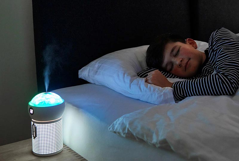 Luftbefeuchter NAYA leuchtet und steht auf dem Nachttisch, im Bett schläft ein Junge seitlich