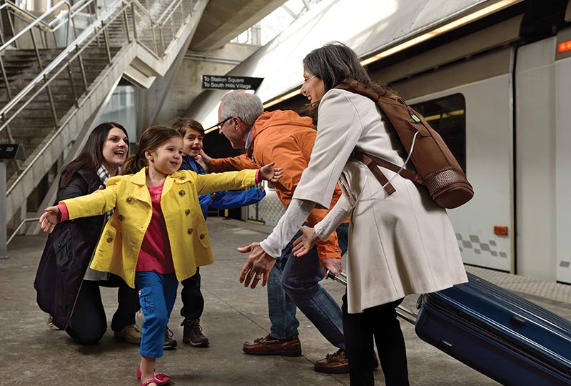 Pärchen begrüßt freudig die Enkelkinder auf einem Bahnsteig, die Dame trägt dabei den SimplyGO Mini Sauerstoffkonzentrator im Rucksack