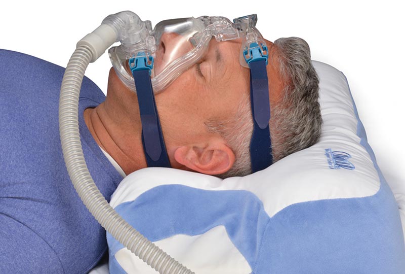 Mann liegt auf dem CPAP Polster mit einer CPAP Maske aufgesetzt und schläft auf  dem Rücken