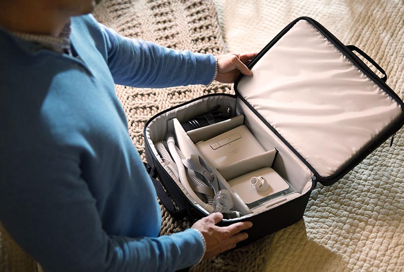 Mann steht vor dem Bett, auf dem Bett liegt die offene Reisetasche mit der Philips DreamStation darin
