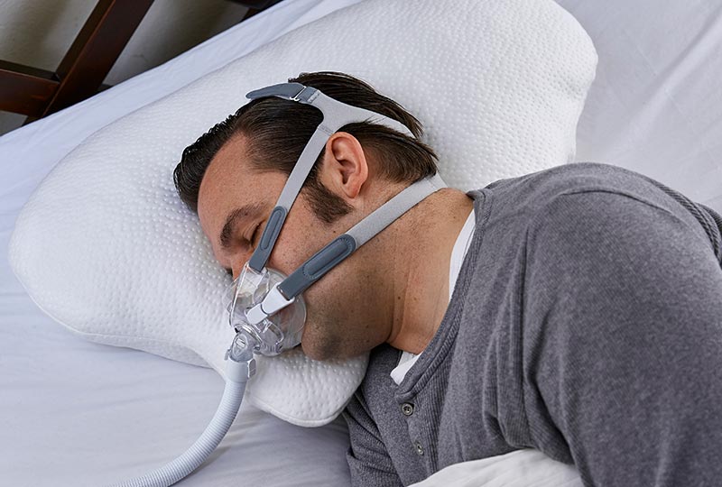 Mann trägt eine CPAP Maske und schläft seitlich auf dem LINA Polster